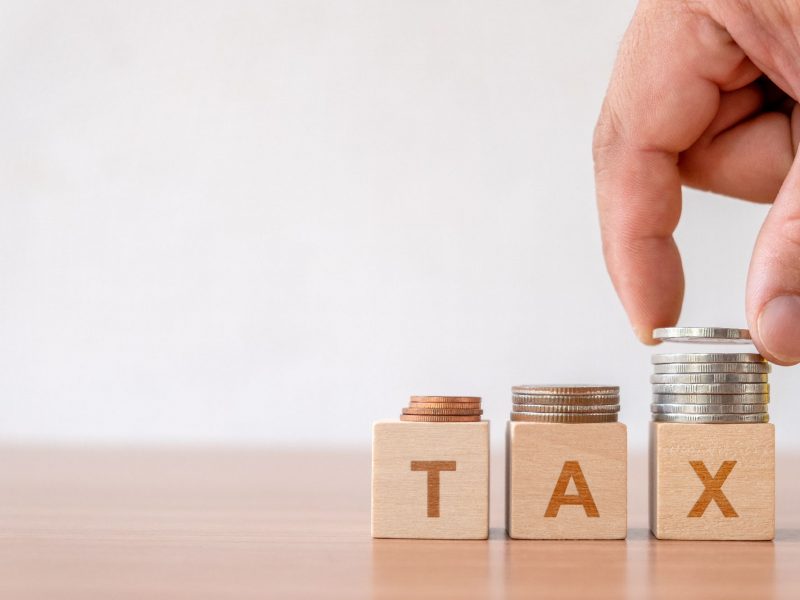 Concept of tax and financial management taxes season in business. Hand putting coins stack step staircase on wooden cube block with  TAX word.